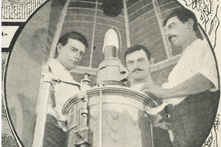 A black and white image from 1912 showing threee men standing around a light inside a lighthouse.