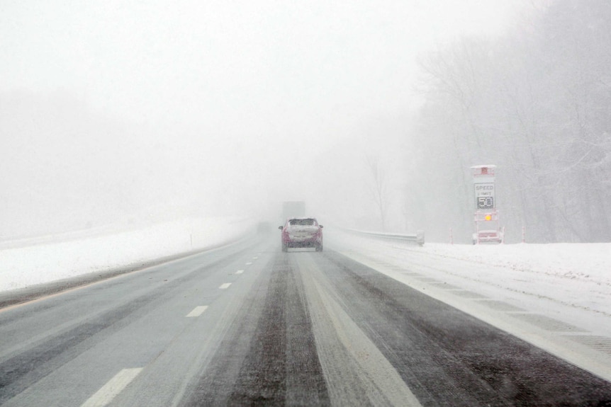 Cars drive along a road in Ohio. Visibility is very low due to heavy snow falls. Only the car directly in front is visible.