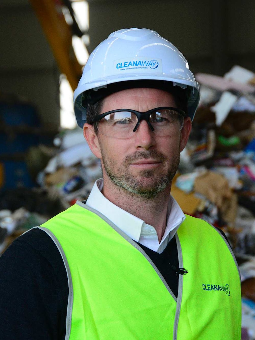 A man in a hard hat and high visibility vest in front of a pile of rubbish