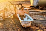 A man sits in a bathtub on a farm