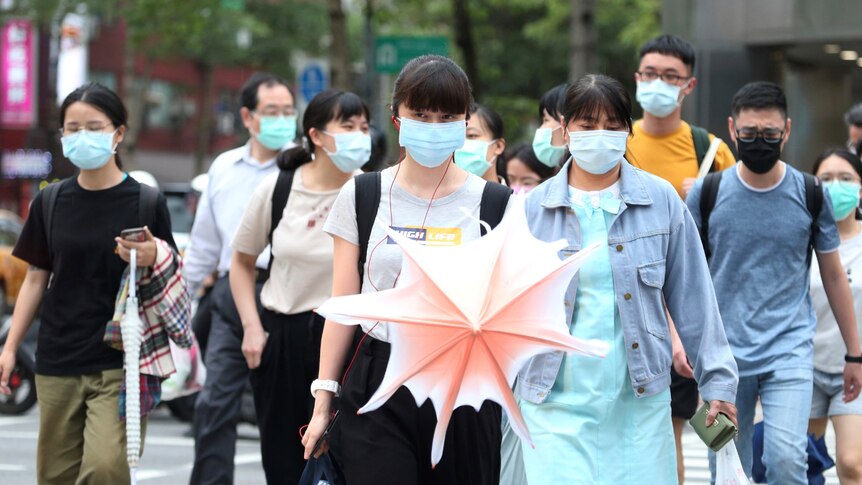 A group of people wearing face masks walks down the street.