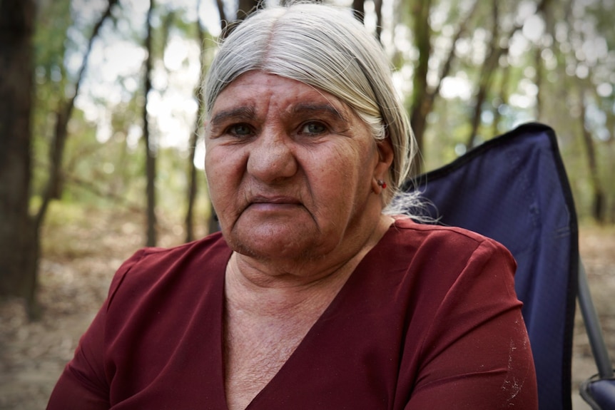 Kathy Herold sits on a camping chair, with gum trees behind her.