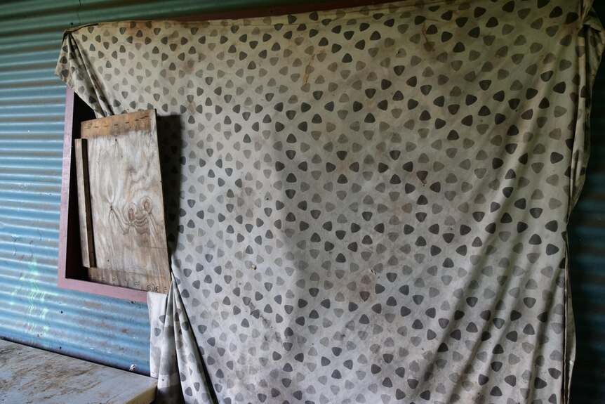 an old blanket and wooden board covers a house window