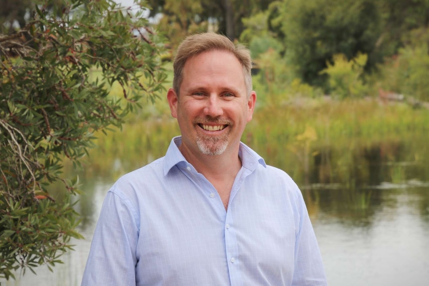 A man in a light blue shirt poses for a photo in front of a swamp