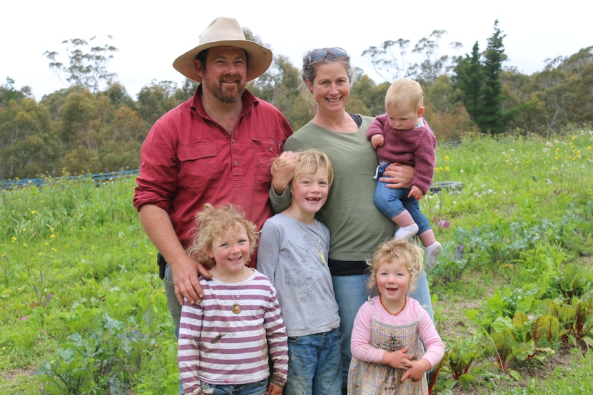 A family of six stand in the middle of their market garden and smile at the camera. 