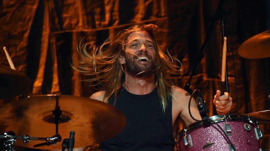 Taylor Hawkins, the drummer for Foo Fighters, plays on stage with a smile on his face.