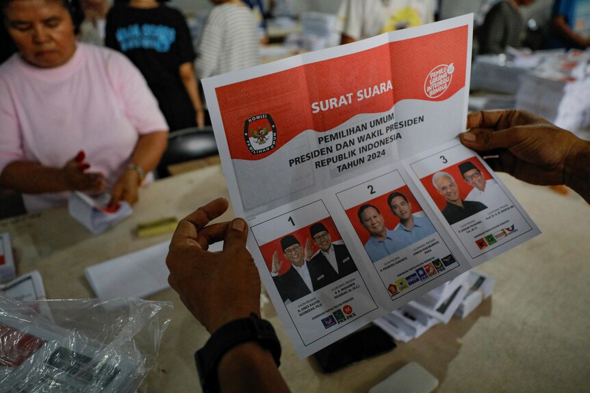 Hands holding a ballot paper with the images of the Indonesian presidential candidates. 