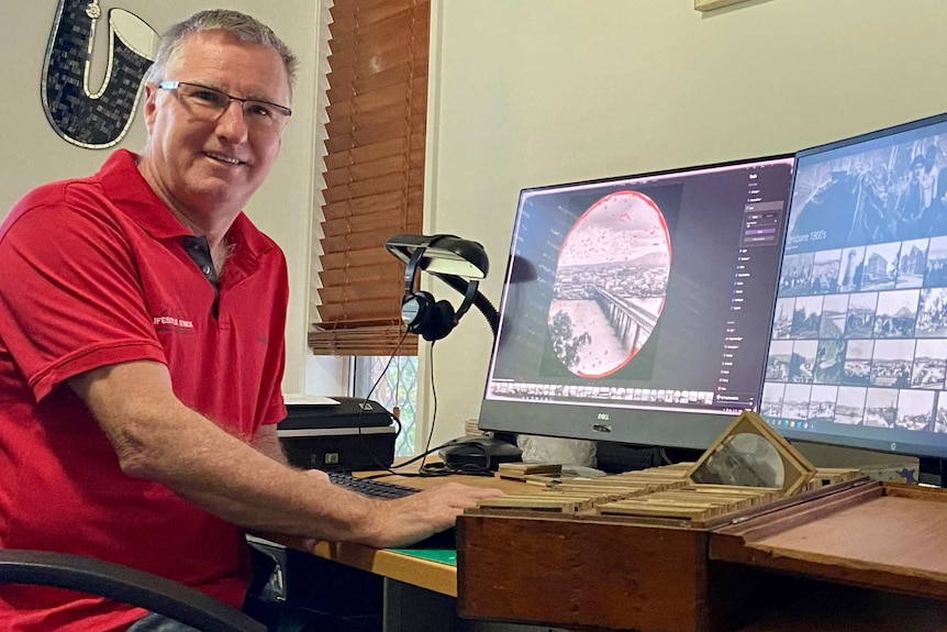 A man sits at his desk. On his computer screens are historic photos that he is restoring.