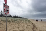 A beach shrouded in rain cloud, a red flag and a sign saying 'danger no swimming'