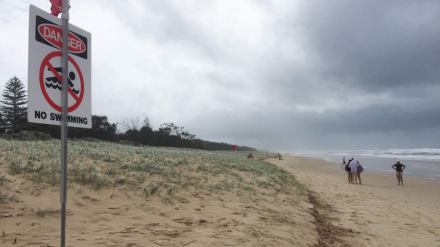 A beach shrouded in rain cloud, a red flag and a sign saying 'danger no swimming'