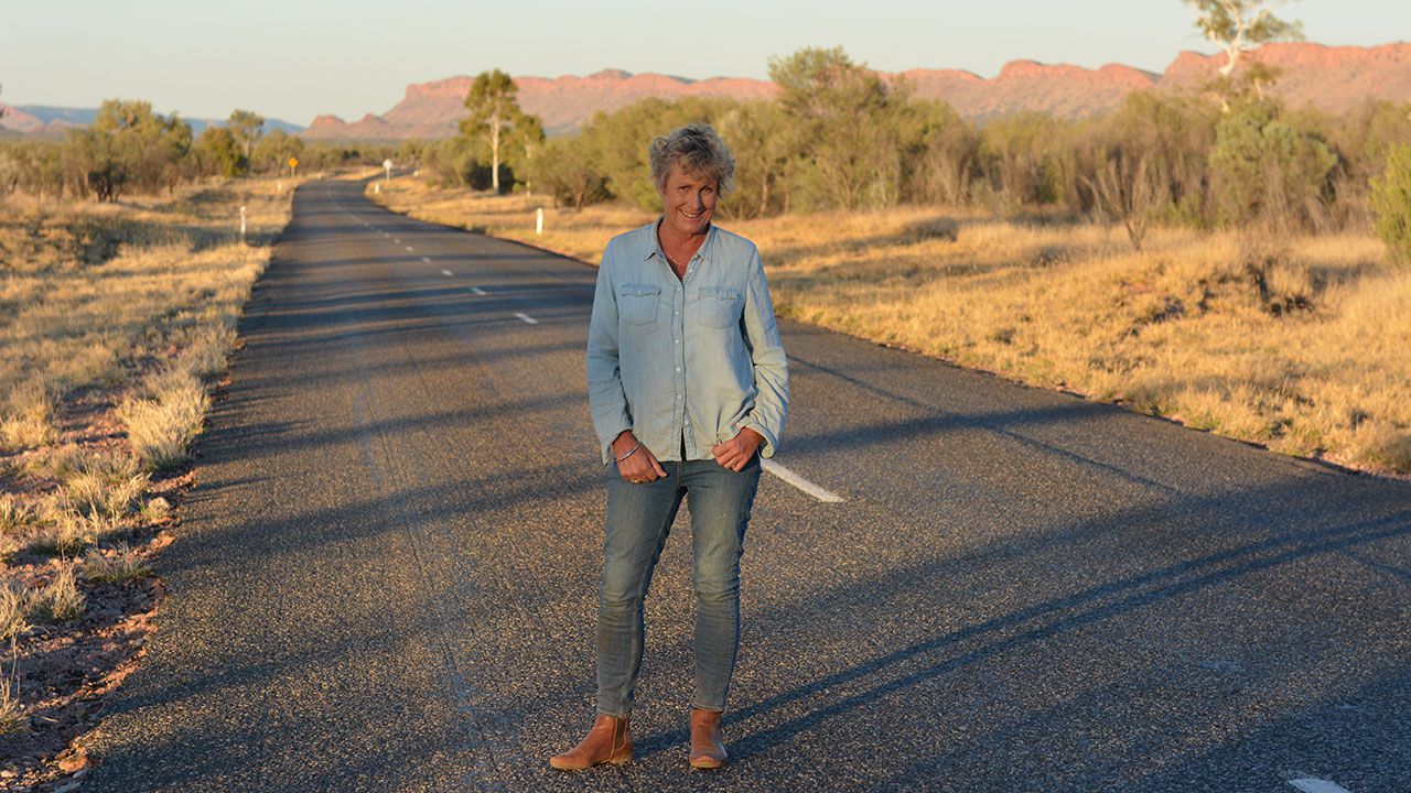 Heather Ewart stands on a country road with hills and trees in background