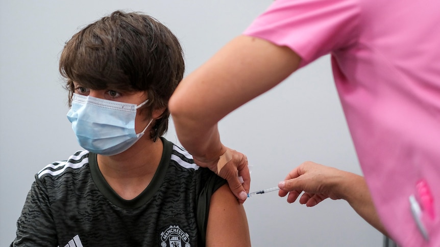 A boy wearing a face mask receives his second dose of the Pfizer vaccine