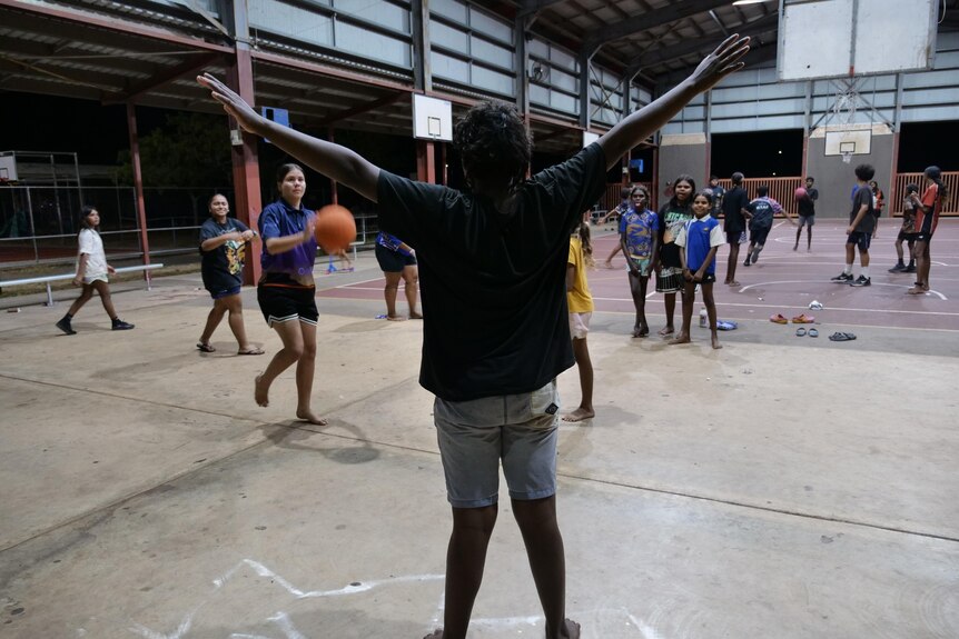 An Indigenous boy pictured from behind lifts his arms in the air on the basketball court