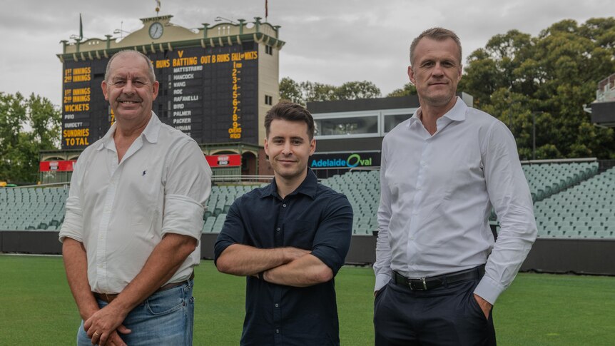 Group of men standing in front of Adelaide Oval scoreboard