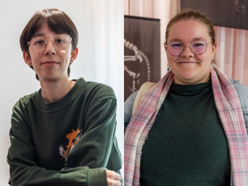  A teenage man in glasses and a green jumper and a teenage woman in glasses and a pink scarf smile into the camera.