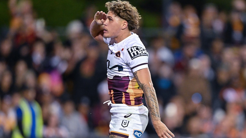 NRL player Reece Walsh standing upright, saluting to the crowd, after scoring a try.