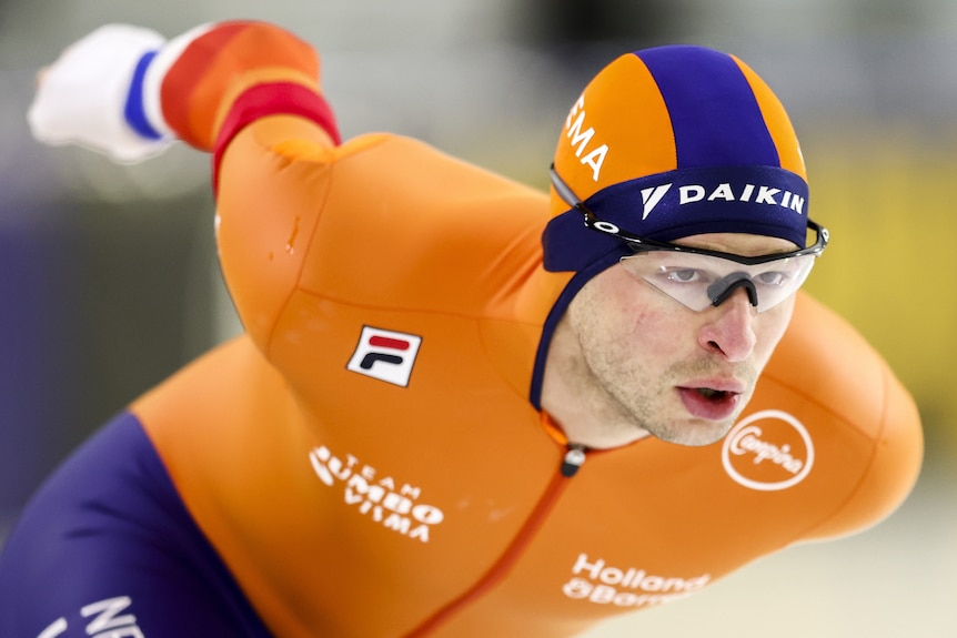 Sven Kramer skates, looking forward through clear glasses wearing an orange bib suit