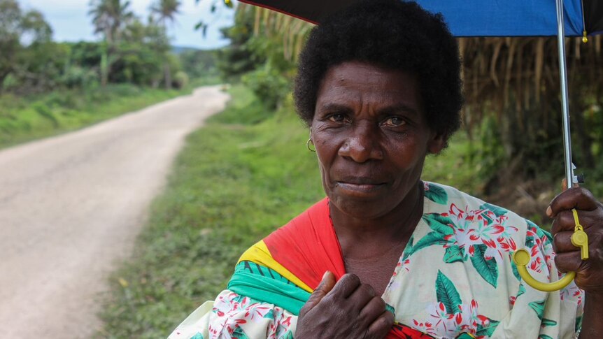 A woman in bright clothing holds an umbrella on the side of a road on the island of Tanna in Vanuatu.