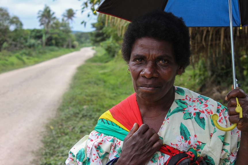 A woman in bright clothing holds an umbrella on the side of a road on the island of Tanna in Vanuatu.