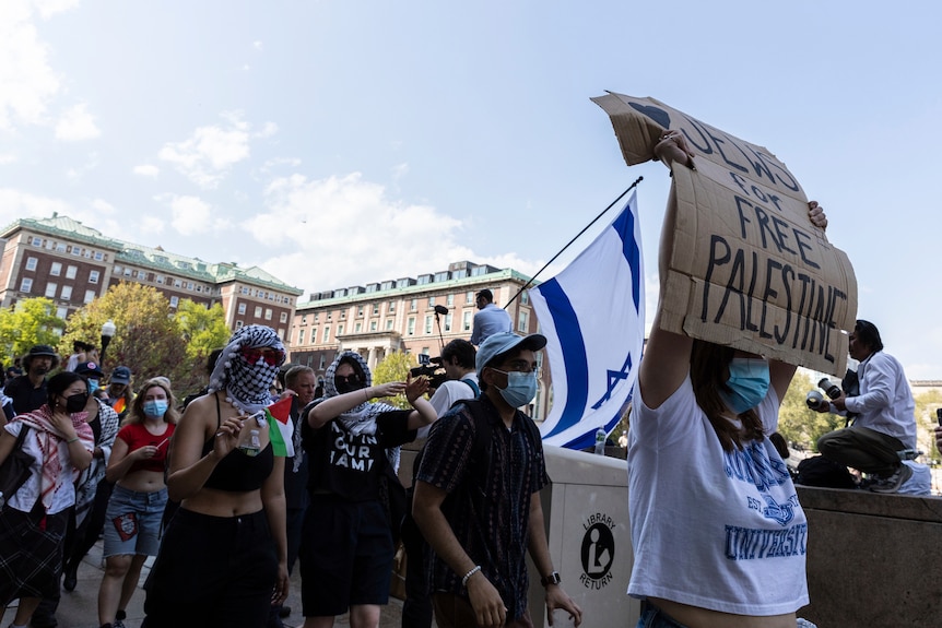 A group of people wearing masks holding up signs and flags.