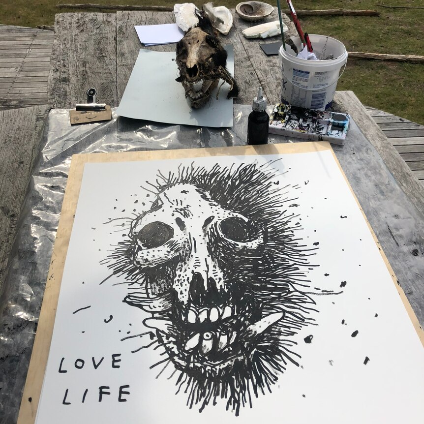 a black painting of a scull, it is in progress on a table outside.