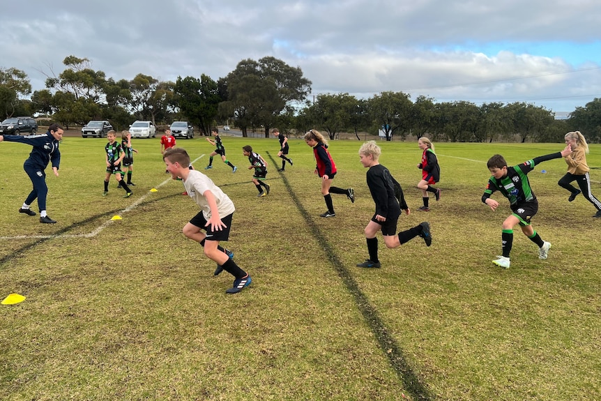 a bunch of kids in soccer kits running on a green oval in a drill.