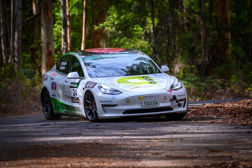 A white car decorated with advertising stickers, driving in a forest