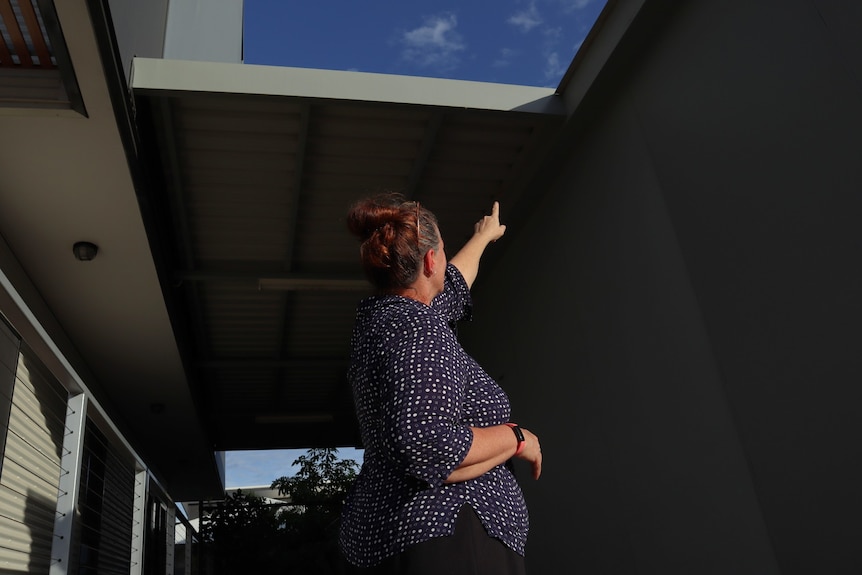 A woman wearing a blue top points up at the ceiling of a residential home.