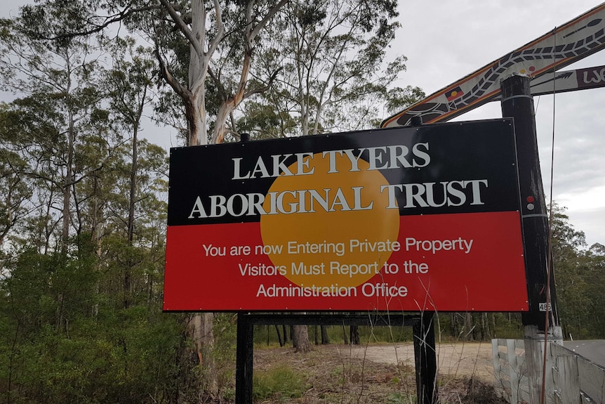 A sign with "Lake Tyers Aboriginal Trust" written on an Aboriginal flag background.