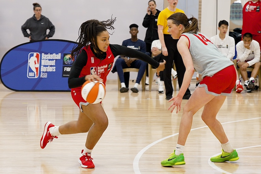 Two women wearing different colors are playing on a basketball court.
