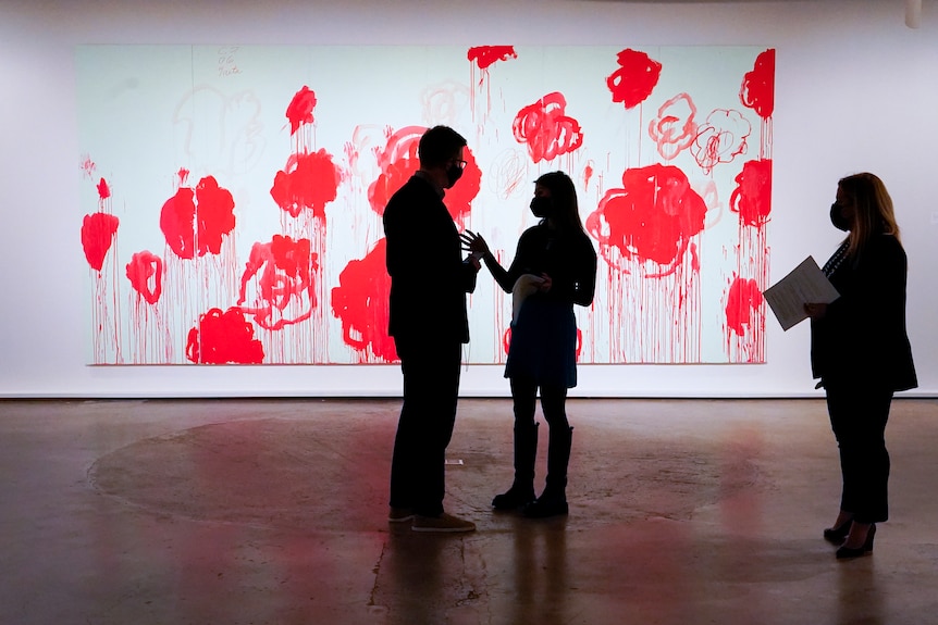 Silhouetted people stand in front of a large painting of red peonies.