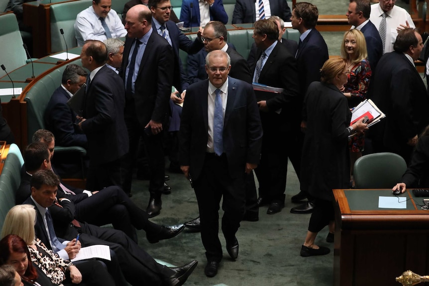 Prime Minister Scott Morrison walks through the House of Representatives and his colleagues walk in another direction.