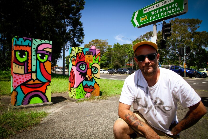 A man stands near two traffic signal boxes he painted in Wollongong.