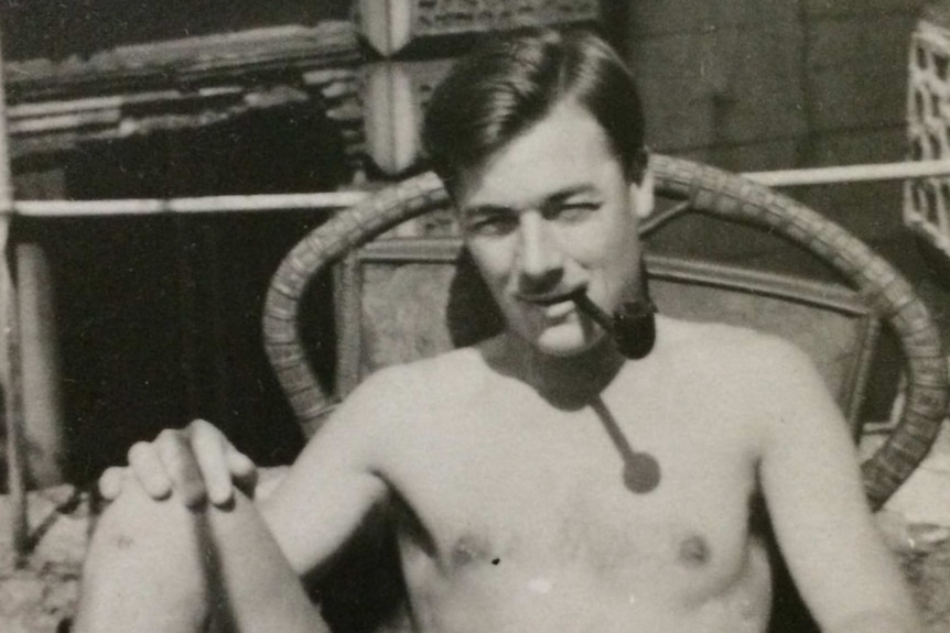 Black and white photo of Bill Rudd relaxing in a chair outside with his feet up and shirt off while smoking a pipe.
