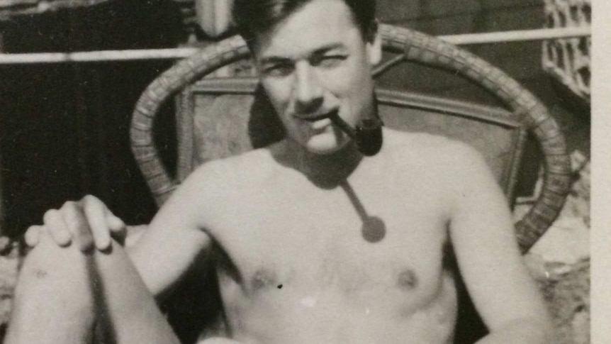 Black and white photo of Bill Rudd relaxing in a chair outside with his feet up and shirt off while smoking a pipe.