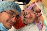 A couple with newborn baby in surgical clothing.