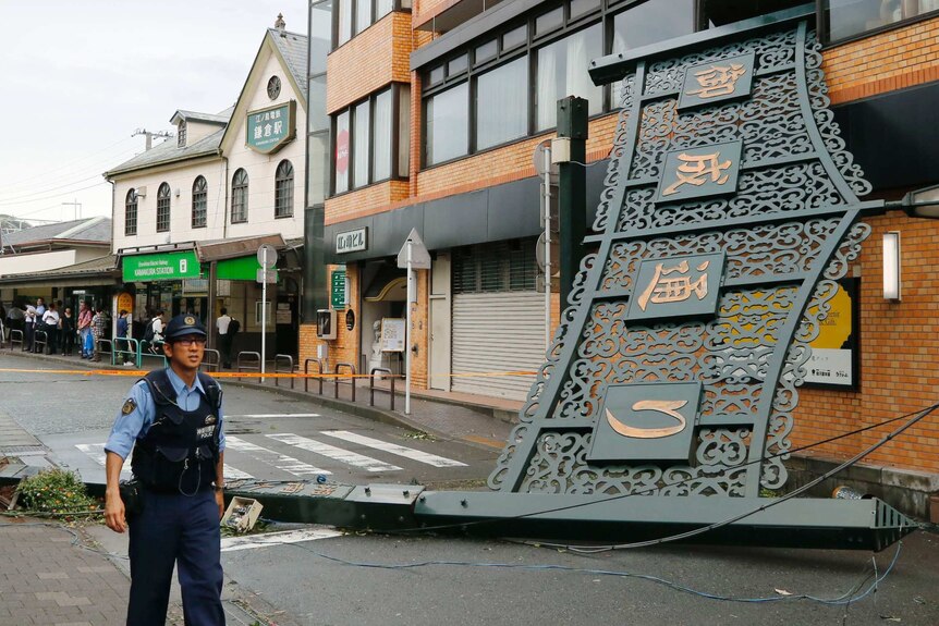 A police officer walks past a fallen signboard hit by typhoon at a shopping district in Kamakura.