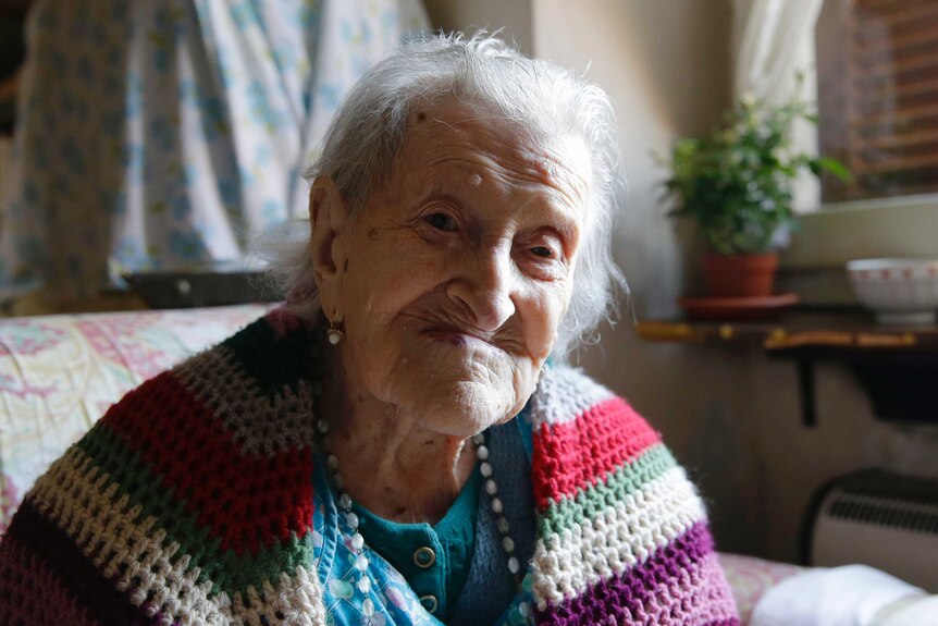 Emma Morano looks at the camera while wearing a multicoloured knitted quilt