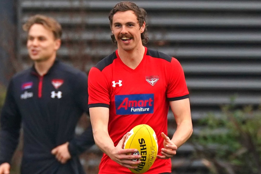 Joe Daniher smiles while holding a football at training
