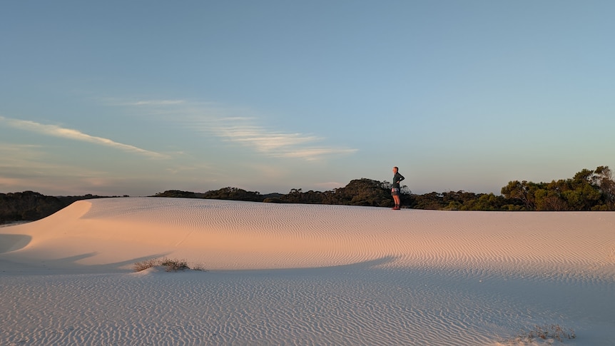 A woman stands on sand dunes.