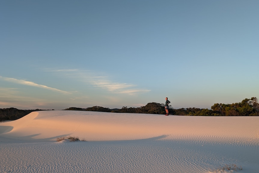 A woman stands on sand dunes.