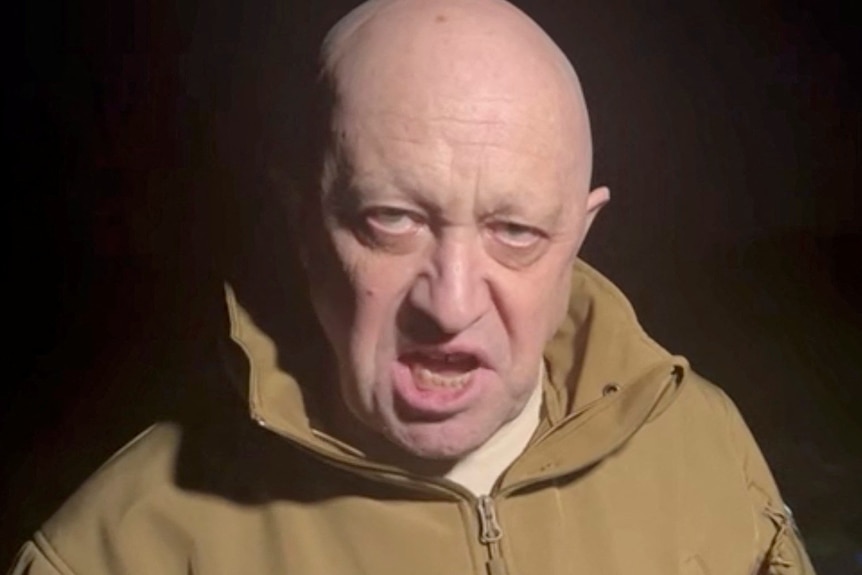 A close up of Yevgeny Prigozhin speaking. He has a bald head and wears a light brown zip-up jacket.