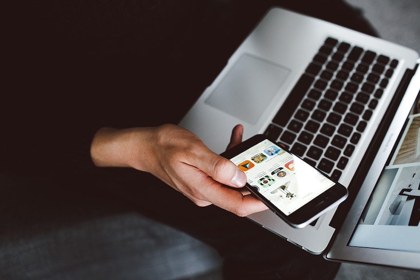 Person holding laptop computer and mobile phone.