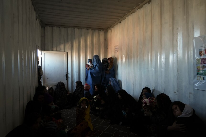 Afghan women sit and stand together in a shipping container. 