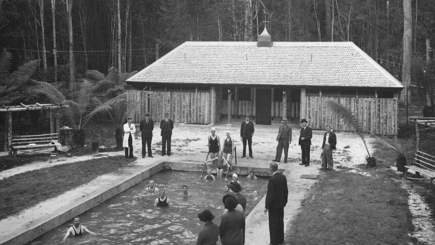 Black and white photo of people standing next to a pool