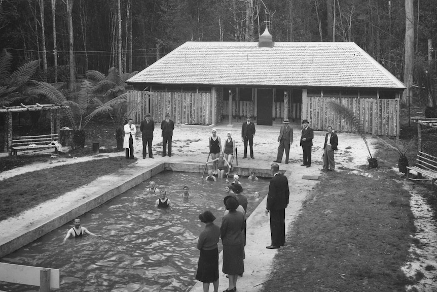 Black and white photo of people standing next to a pool
