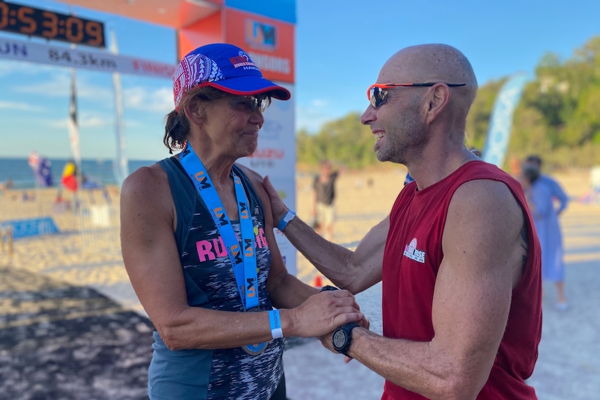 A woman and a man hold hands at the finish line of a race on a beach 