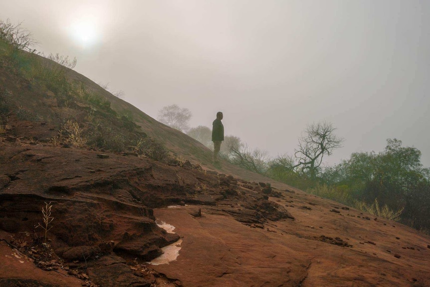 Silhouette of Aaron Pedersen standing on a steep slope.
