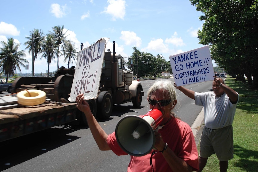 Activists hold their placards up to passing traffic on a busy road.