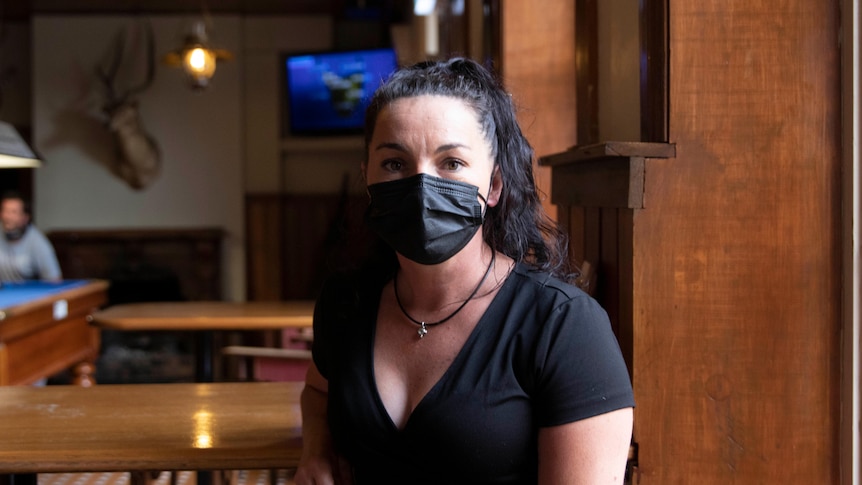 woman with dark hair wearing a mask sits at a table at a pub